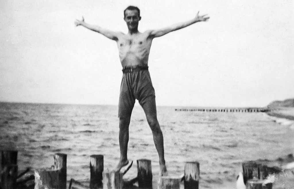 Ein junger Mann steht mit ausgebreiteten Armen auf den Bohlen der Ostsee.