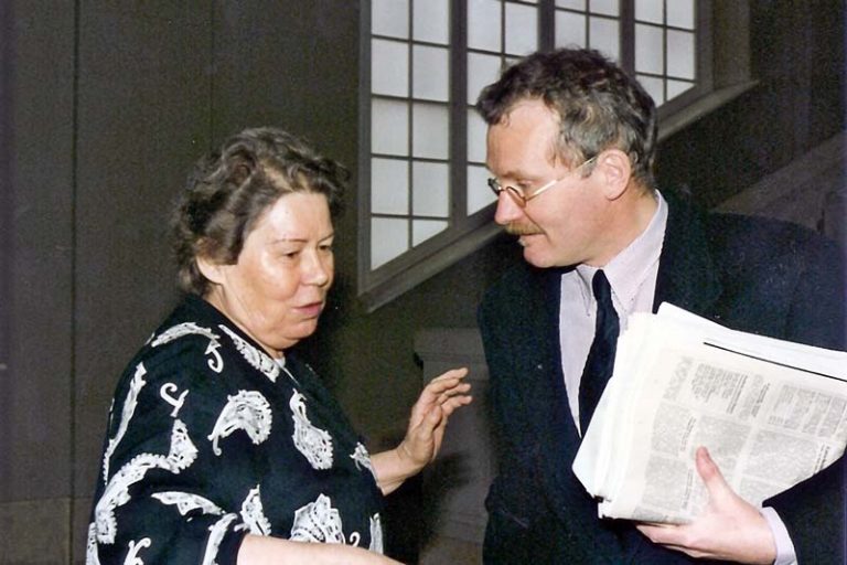 Dr. Emmi Wolf und Professor Hermann Haarmann, der eine Zeitung in der Hand hält. Sie unterhalten sich.