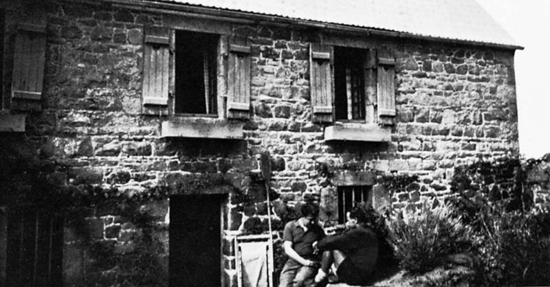 Zwei Menschen sitzen vor einem sch&ouml;nen Steinhaus mit Fensterl&auml;den.