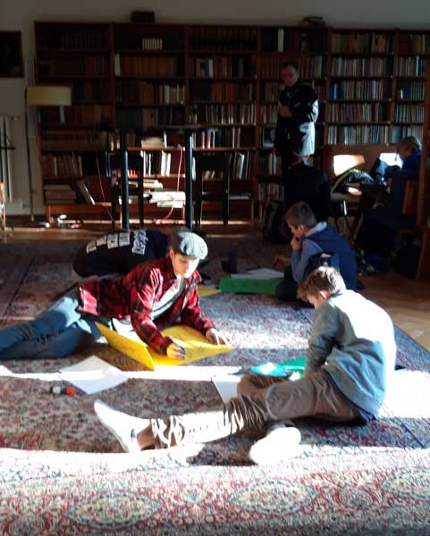 Zwei Jugendliche sitzen auf einem Teppich in einer Bibliothek an einem Projekt