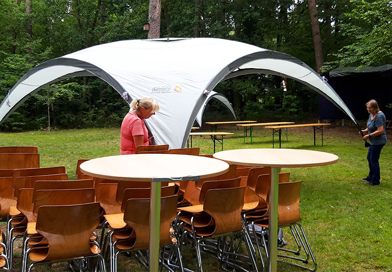 Zwei Frauen bauen Tische, Stühle und Sonnenschutz für eine Veranstaltung im Garten auf