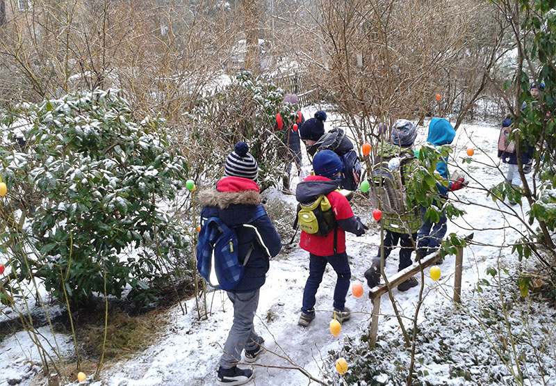 Kinder spazieren in Winterlandschaft mit Ostereiern