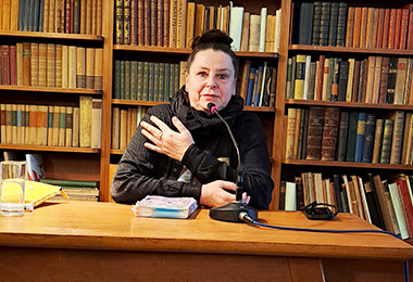 Annette Gröschner sitzt vor einem Bücherregal und liest aus ihrem Buch vor.